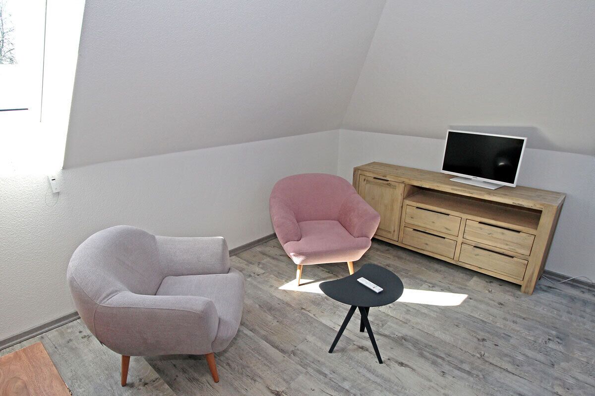Una habitación con un armario de madera, un televisor, dos sillas y una mesita.