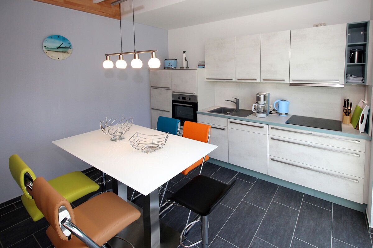 A modern kitchen with white cabinets, a white countertop, and a dining area with a white table and chairs.