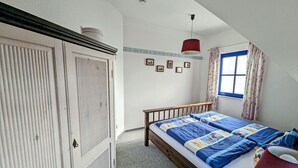 A bedroom with a bed, a wardrobe, a window with curtains, and a red hanging lamp. - Vacation home with a fireplace and an infrared sauna, about 200 meters from the sandy beach (Glowe)