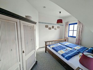 Ein Schlafzimmer mit Bett, Kleiderschrank, einem Fenster mit Vorhängen und einer roten Hängelampe.