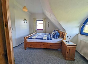 A bedroom with a wooden bed, a nightstand, a window with curtains, and a ceiling with a sloped design. - Vacation home with a fireplace and an infrared sauna, about 200 meters from the sandy beach (Glowe)