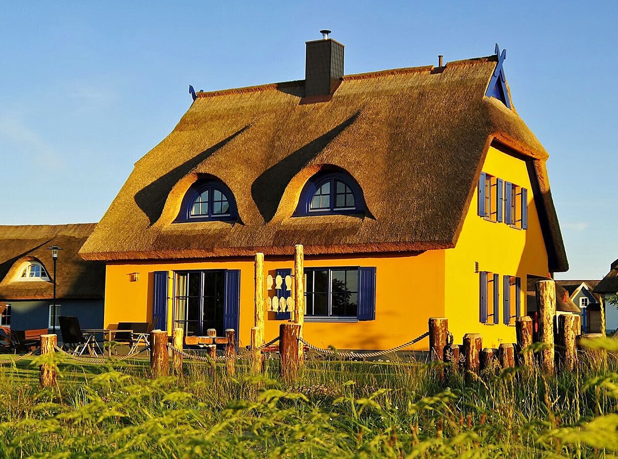 A thatched-roof house with a yellow facade and multiple windows.