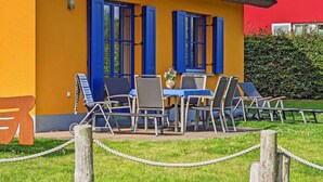 A yellow building with blue shutters and a thatched roof, featuring outdoor seating with chairs and a table. - Vacation home with a fireplace and an infrared sauna, about 200 meters from the sandy beach (Glowe)
