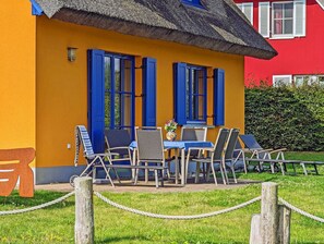 Ein gelbes Gebäude mit blauen Fensterläden und einem Strohdach, mit Außenplätzen, inklusive Stühle und Tisch.
