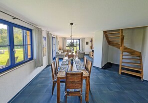 A spacious dining area with a long table and chairs, a staircase, and large windows offering a view of the outdoors. - Vacation home with a fireplace and an infrared sauna, about 200 meters from the sandy beach (Glowe)
