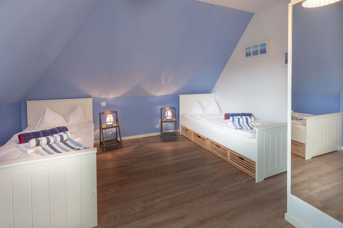 Une chambre avec deux lits, un plancher en bois et un plafond en pente.