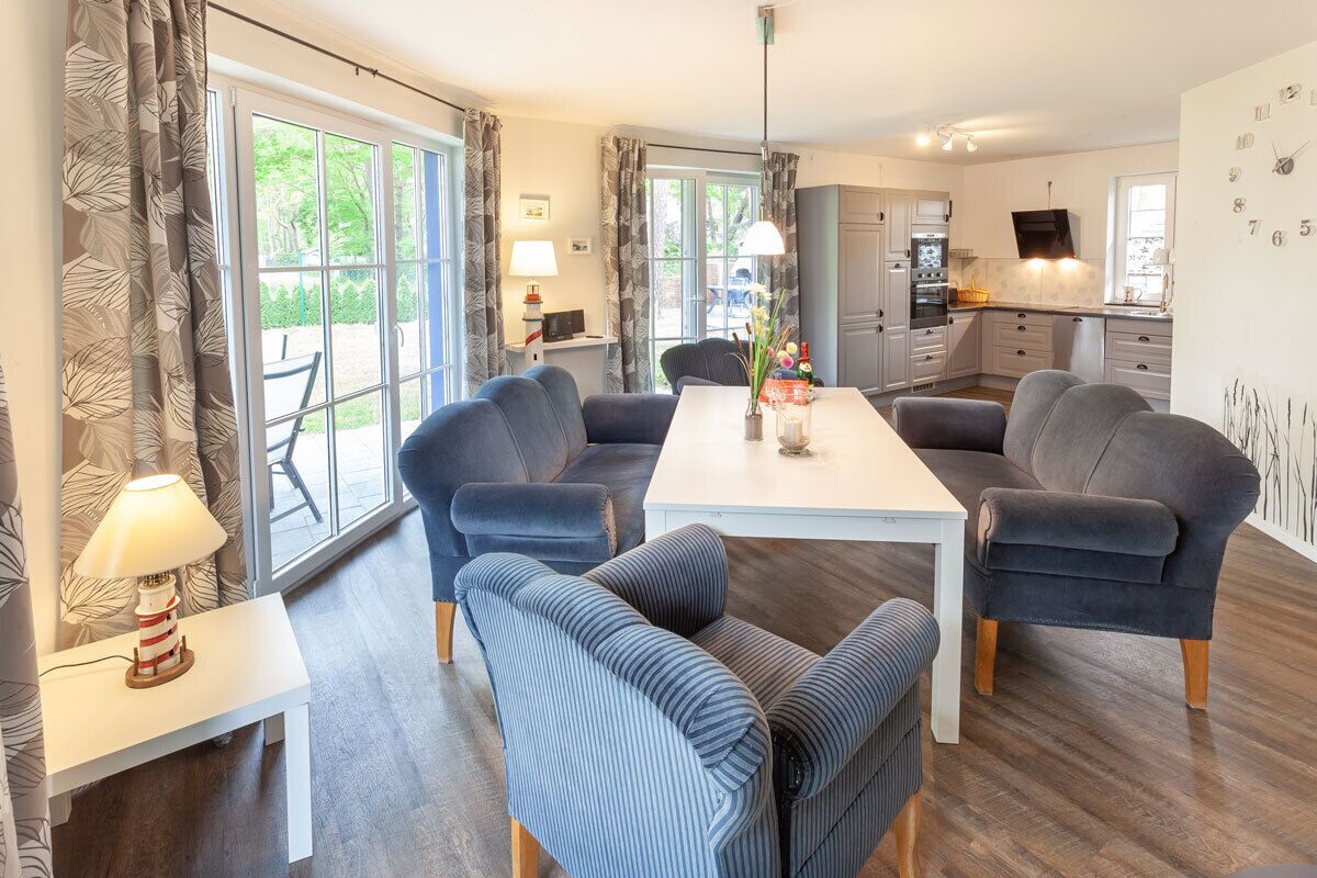 A modern living room with a dining table, sofas, and a kitchen in the background.