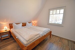 A bedroom with a wooden bed, two bedside tables with lamps, a window with a view of trees, and a sloped ceiling. - Vacation home with a fireplace, about 400 meters from the sandy beach, 2 bedrooms, sleeps up to 5 people (Glowe)