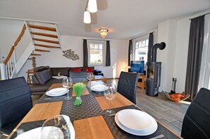 A dining area with a wooden table set for four, a sofa, a television, and a wood-burning stove. - Vacation home with a fireplace, about 400 meters from the sandy beach, 2 bedrooms, sleeps up to 5 people (Glowe)