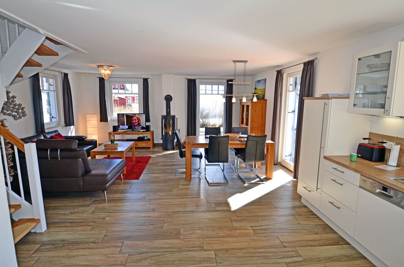 Ein modernes Wohnzimmer mit Sofa, Esstisch und Stühlen, einer Küchenzeile mit Schränken und Geräten sowie einem großen Fenster für natürliches Licht.