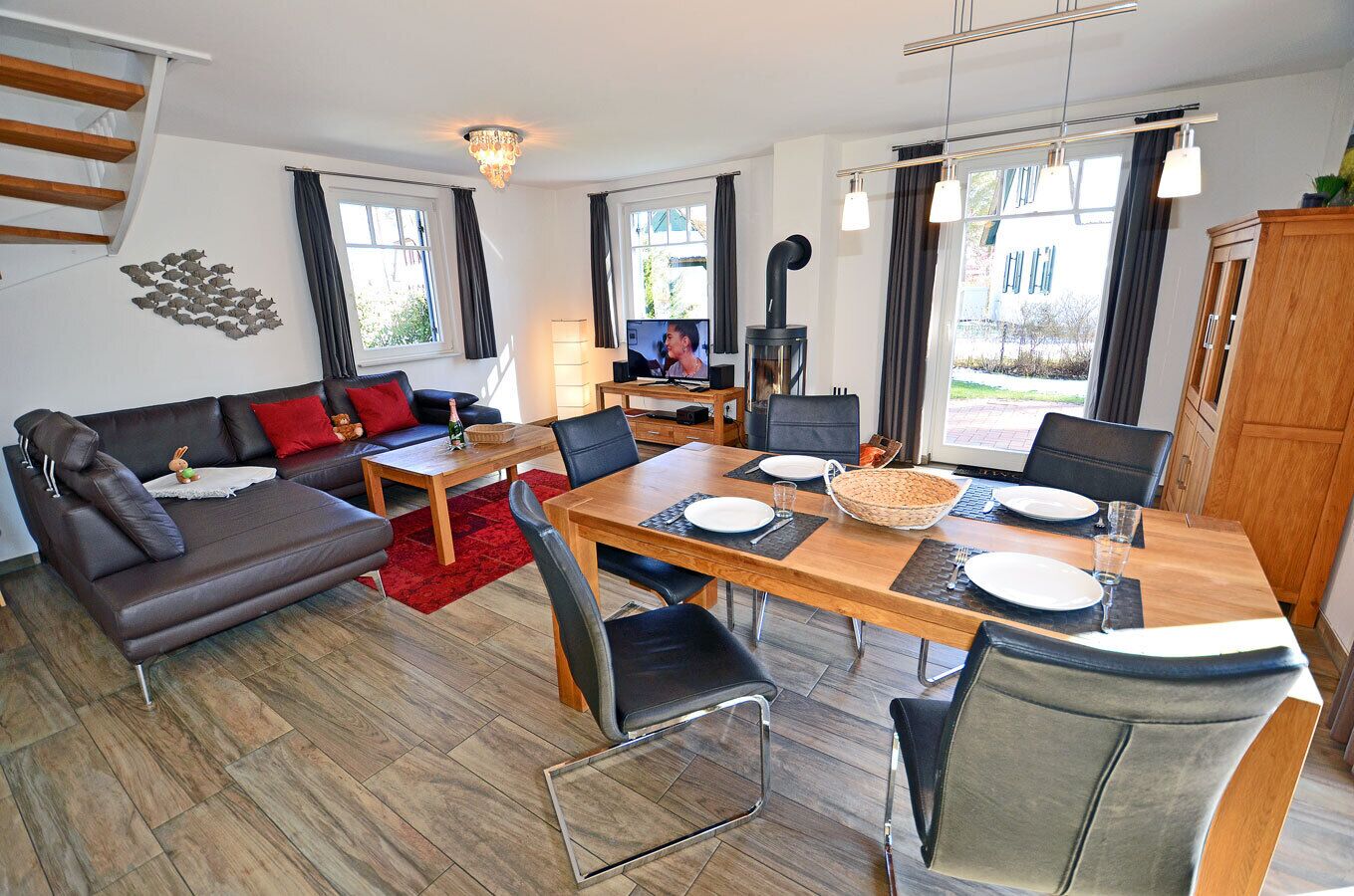 A modern living room with a sofa, dining table, and chairs, a fireplace, and a staircase.