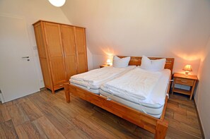 A bedroom with a double bed, wooden wardrobe, bedside tables, and a door. - Vacation home with a fireplace, about 400 meters from the sandy beach, 2 bedrooms, sleeps up to 5 people (Glowe)