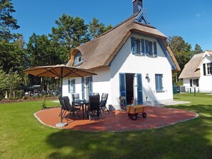 A white house with a thatched roof, a patio with outdoor furniture, and a small garden. - Vacation home with a fireplace, about 400 meters from the sandy beach, 2 bedrooms, sleeps up to 5 people (Glowe)