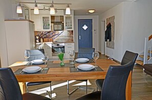 A dining area with a wooden table set for four, surrounded by chairs, and a kitchen in the background. - Vacation home with a fireplace, about 400 meters from the sandy beach, 2 bedrooms, sleeps up to 5 people (Glowe)