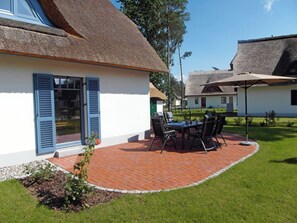 A house with a thatched roof, a patio with a table and chairs, and a small garden area. - Vacation home with a fireplace, about 400 meters from the sandy beach, 2 bedrooms, sleeps up to 5 people (Glowe)