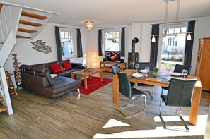 A modern living room with a sofa, dining table, chairs, a fireplace, and a staircase. - Vacation home with a fireplace, about 400 meters from the sandy beach, 2 bedrooms, sleeps up to 5 people (Glowe)