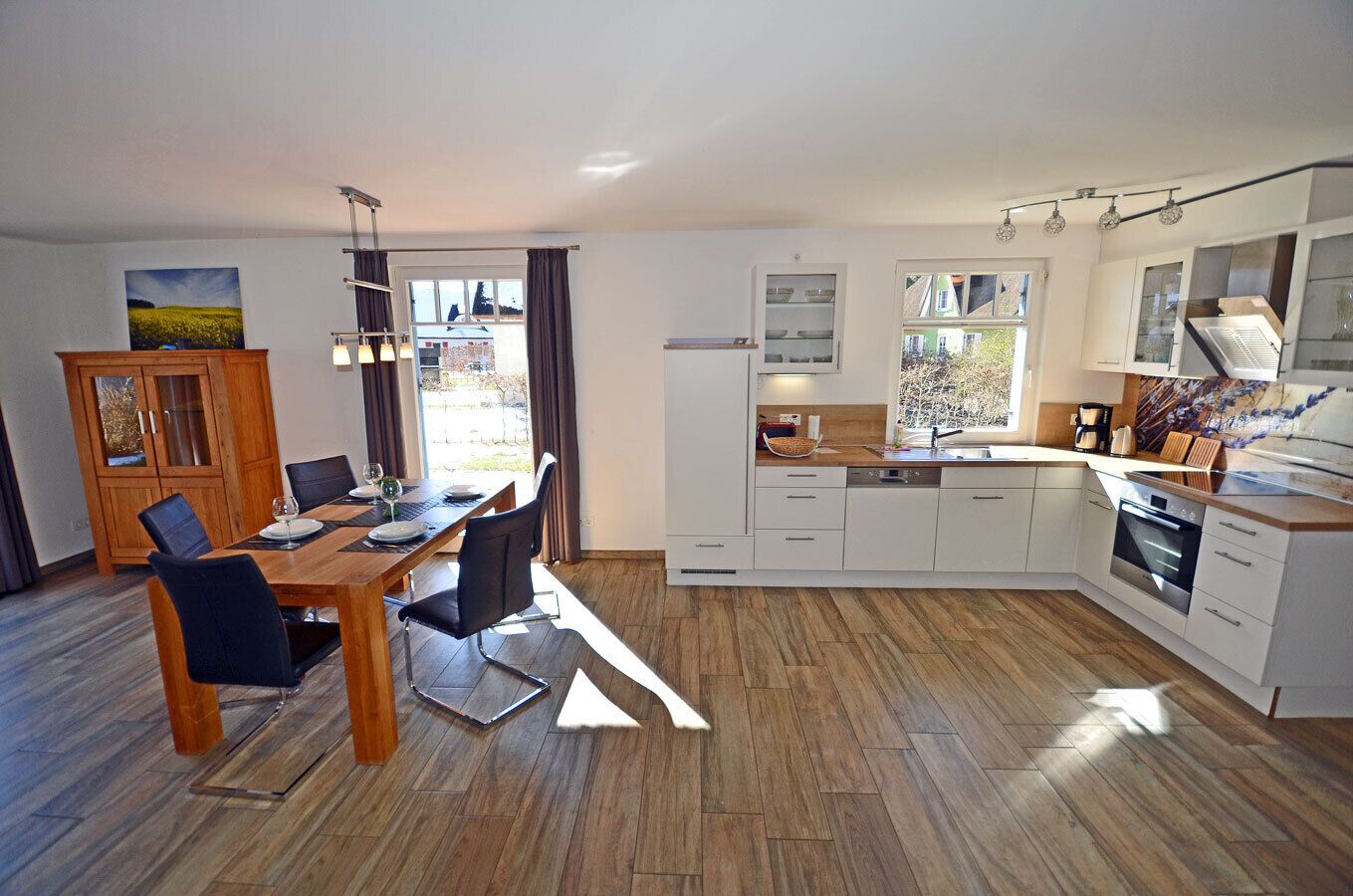 A modern kitchen with white cabinets, a wooden dining table, and a view of the outdoors.