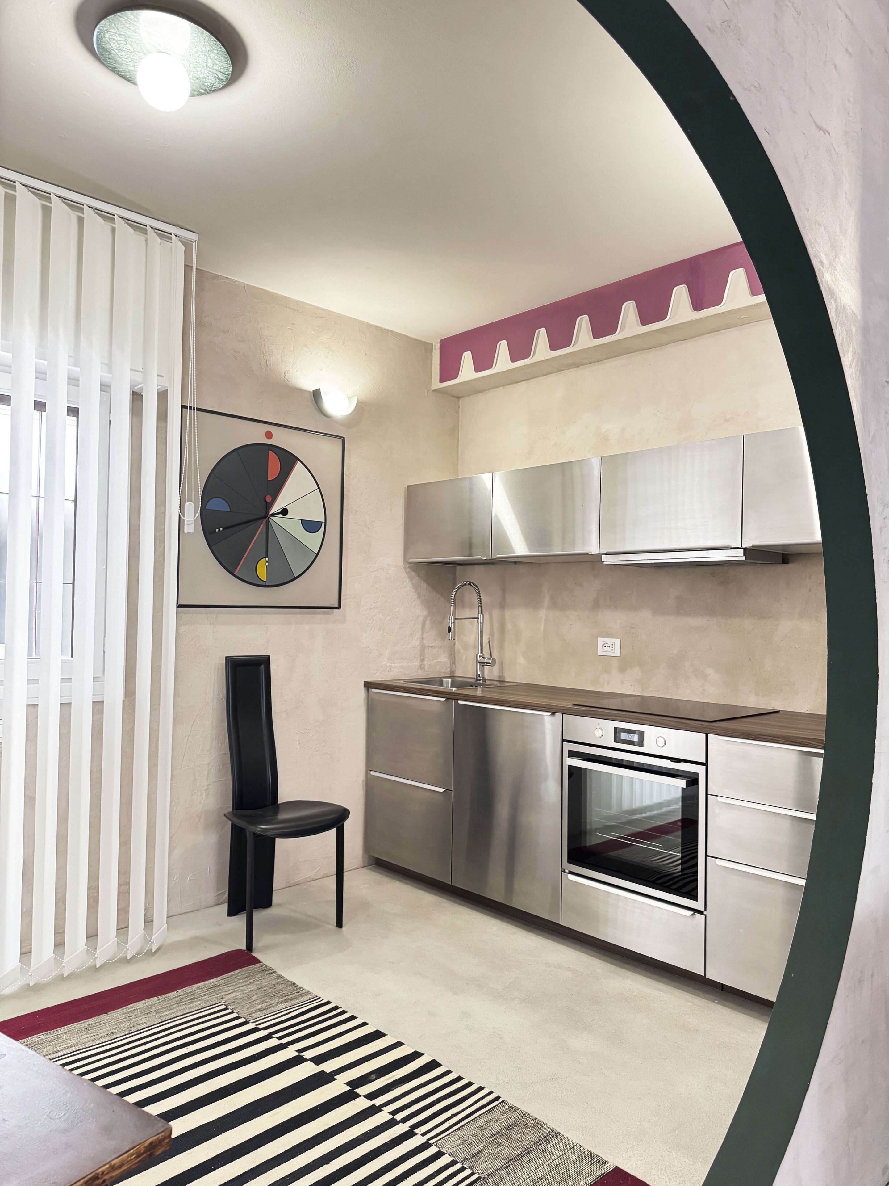 A modern kitchen with stainless steel appliances, a black chair, and a striped rug.