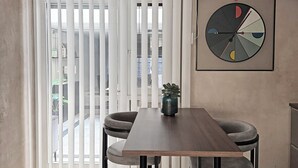 A modern dining area with a table, chairs, a hanging light fixture, a window with blinds, and a wall-mounted clock. - La Bauhaus by Wonderful Italy (Desenzano del Garda)