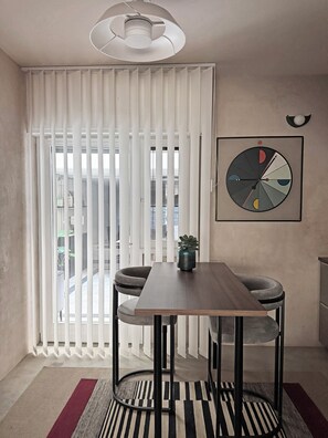 Ein stilvoller Essbereich mit Tisch, Stühlen, einer Hängelampe, einem Fenster mit Jalousien und einer Wanduhr.