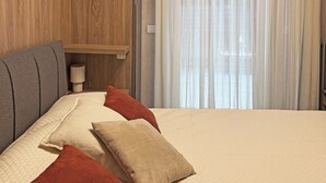 A hotel room with a bed, pillows, a bedside table with a lamp, a wooden shelf, and a window with curtains. - La Bauhaus by Wonderful Italy (Desenzano del Garda)