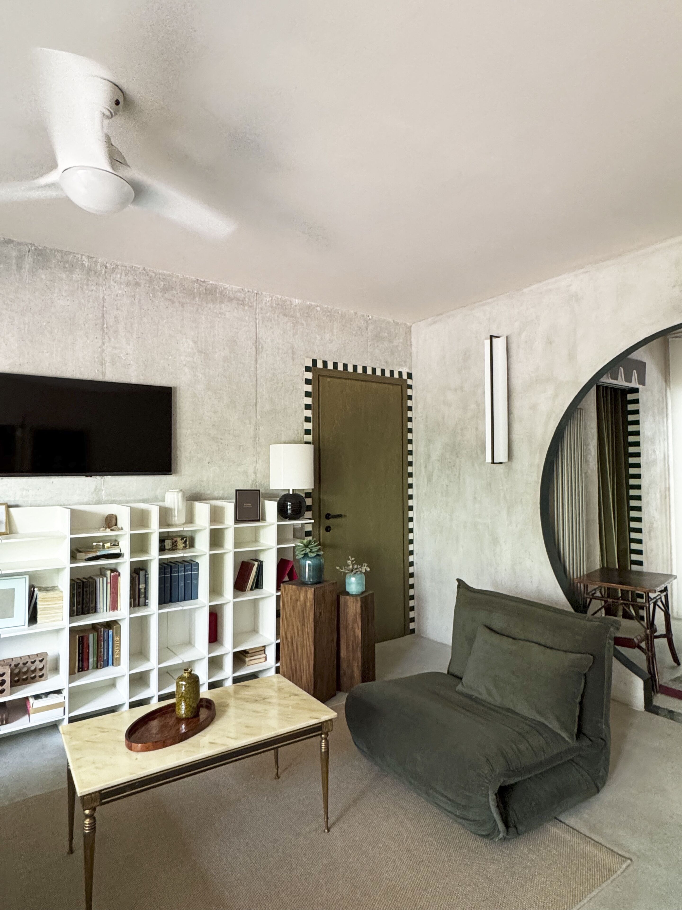 A modern living room with a sofa, a coffee table, a bookshelf, a flat-screen TV, and a round mirror.