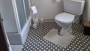 A bathroom with a toilet, a towel rack, a roll of toilet paper, and a patterned floor. - TOWNHOUSE, 2 minutes from the river, with shops and a small courtyard filled with flowers (Barrou)