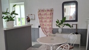 A dining area with a round table, two chairs, a black rug, a white cabinet, and a window with a plant. - TOWNHOUSE, 2 minutes from the river, with shops and a small courtyard filled with flowers (Barrou)