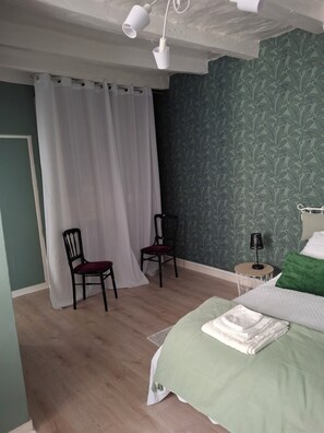 Ein Schlafzimmer mit einem Bett, zwei Stühlen, einem kleinen Tisch mit einer Lampe und einem Vorhang.