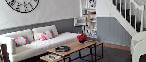 A modern living room with a white sofa, a coffee table, a white chair, a clock, and a staircase.