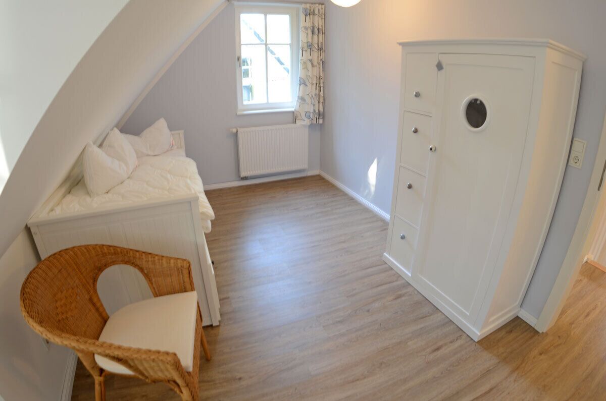 A bedroom with a bunk bed, a chest of drawers, a wicker chair, and a window with curtains.