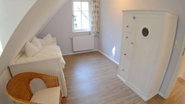A bedroom with a bunk bed, a chest of drawers, a wicker chair, and a window with curtains. - Vacation home with a fireplace and sauna, about 250 meters from the sandy beach, Wi-Fi, washing machine (Glowe)