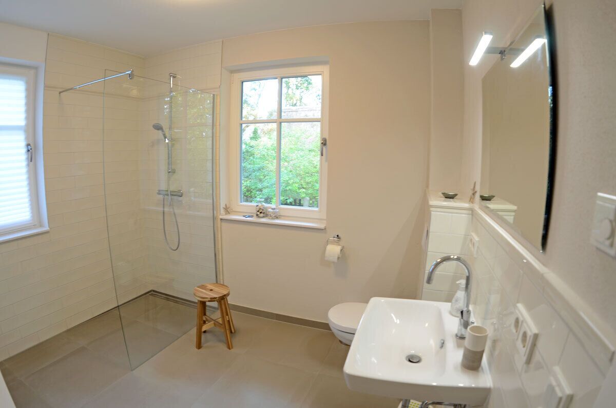 Ein Badezimmer mit Duschkabine aus Glas, Toilette, Waschbecken und Fenster mit Blick auf Grünflächen.