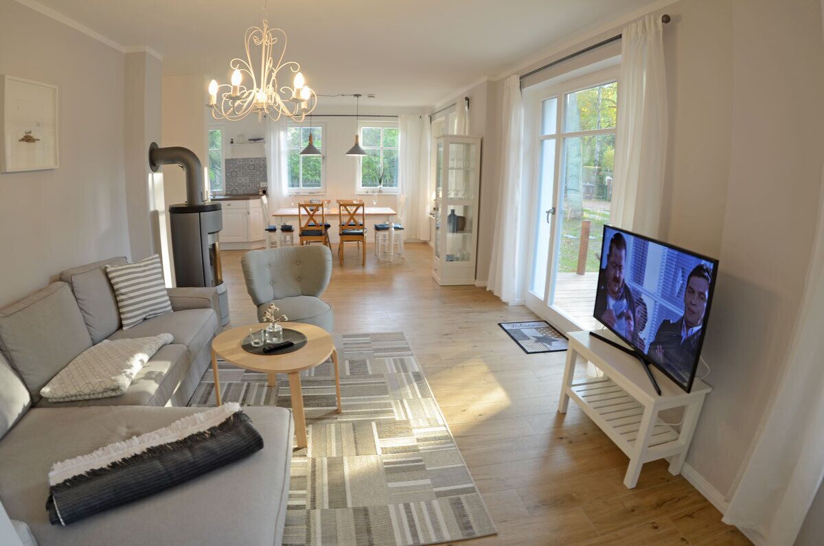 Ein modernes Wohnzimmer mit Sofa, Couchtisch, Fernseher und einem Essbereich im Hintergrund.