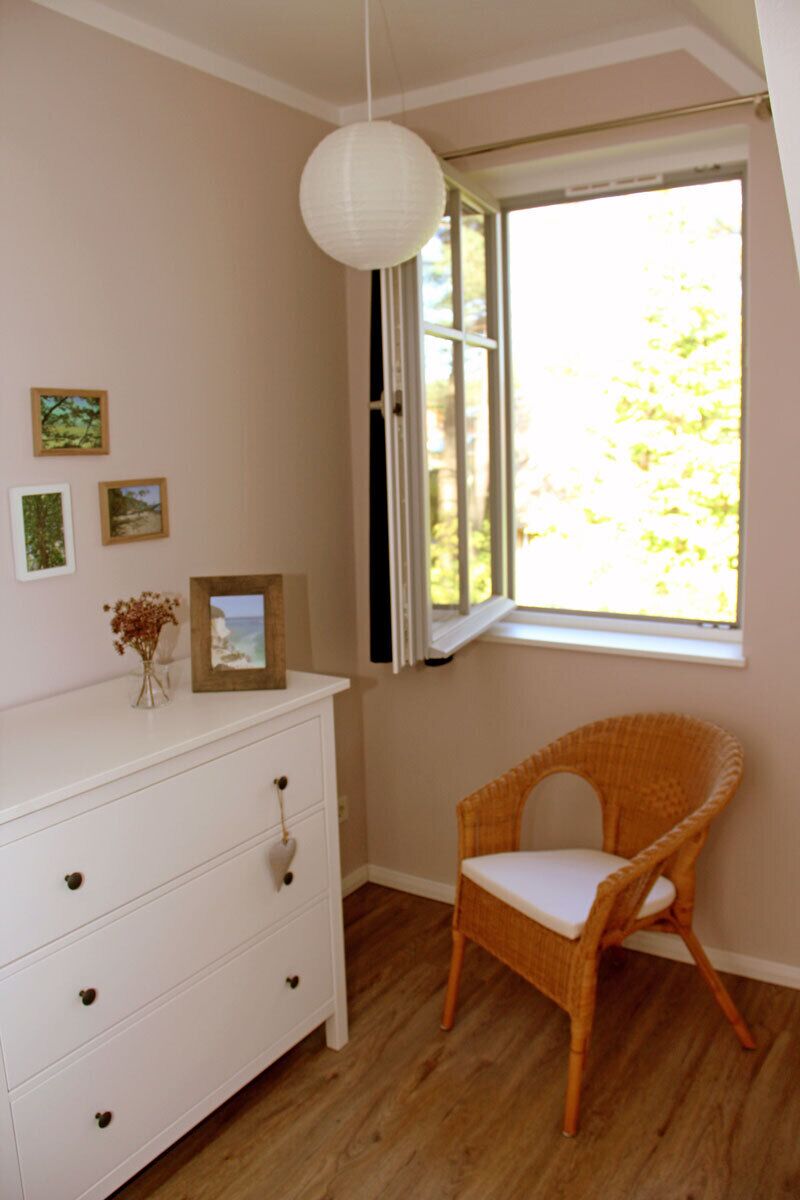Een kamer met een witte dressoir, rieten stoel en een raam met jaloezieën.