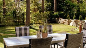 An outdoor deck with a table and chairs, surrounded by trees and a grassy area. - Vacation home with a fireplace and sauna, about 250 meters from the sandy beach, Wi-Fi, washing machine (Glowe)