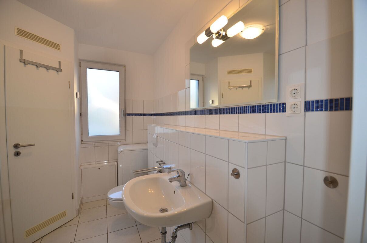 Ein Badezimmer mit einem weißen Waschbecken, einem Spiegel und einem Fenster.
