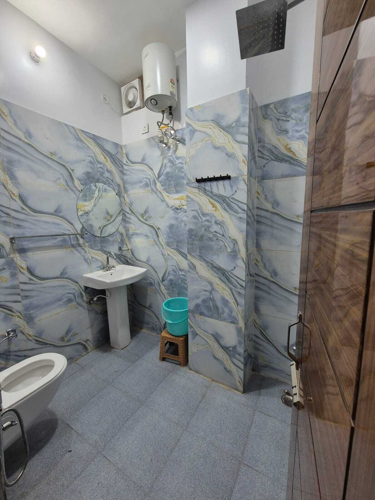 Une salle de bain avec des murs en marbre, un lavabo sur colonne, des toilettes et un espace douche.
