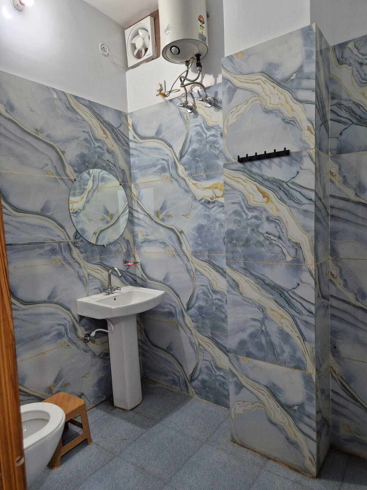 A bathroom with a marble wall, a sink, a toilet, and a shower.