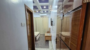 A hallway with a ceiling fan, a bed, a wooden bench, and a wall-mounted TV. - Prince Hotel (Meerut)