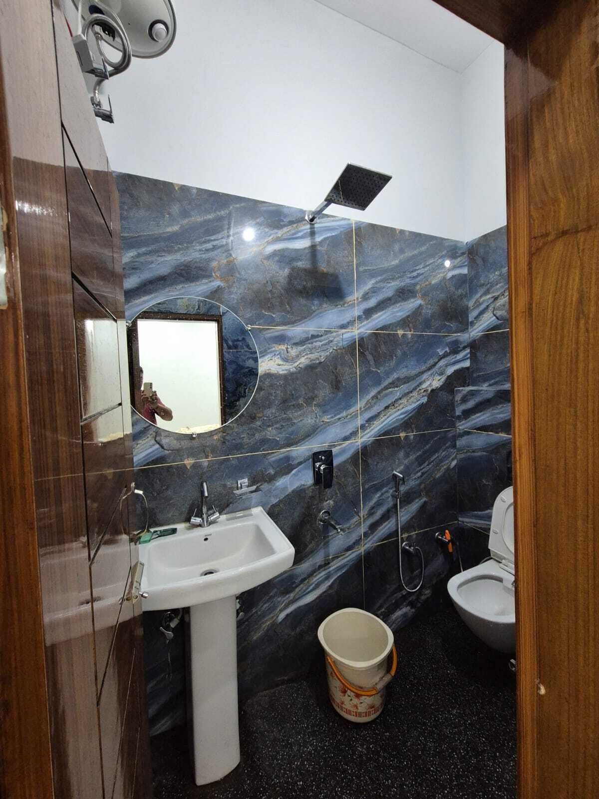 Un baño con pared de mármol, un lavamanos, un inodoro y un balde.