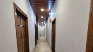 A corridor with wooden doors and a tiled floor, leading to a room with a wooden ceiling and recessed lighting. - Prince Hotel (Meerut)