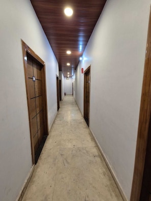 Un pasillo con puertas de madera y suelo de baldosas, que conduce a una habitación con techo de madera e iluminación empotrada.