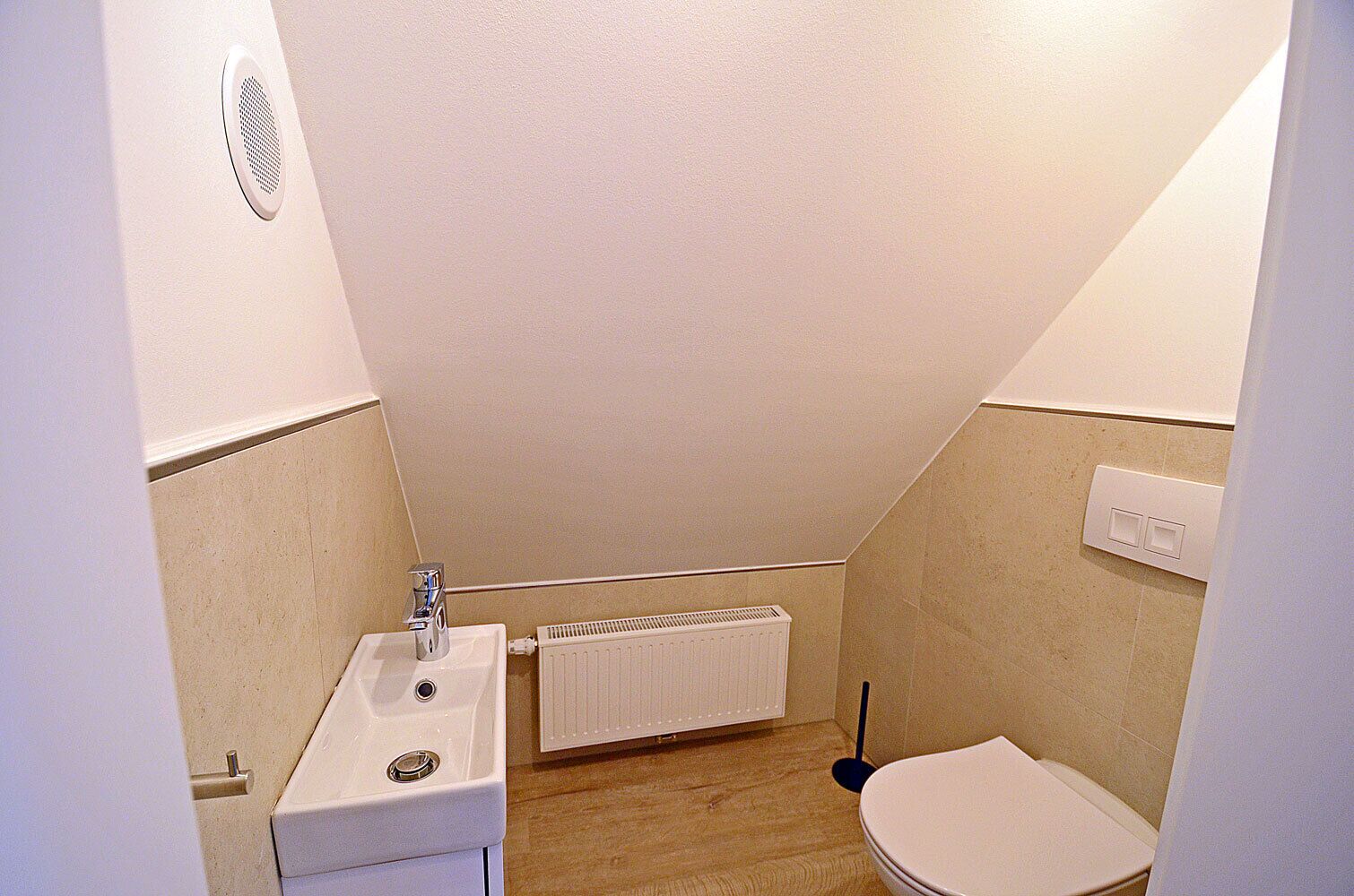 Une petite salle de bain étroite, équipée de toilettes, d’un lavabo et d’un radiateur.