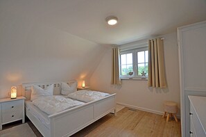 A bedroom with a bed, bedside tables, a window with curtains, a small stool, and a ceiling light. - House with a fireplace and sauna, about 1,300 m from a sandy beach, 4 bedrooms, sleeps up to 8, Wi-Fi (Glowe)