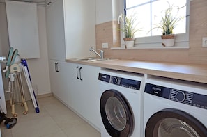 A laundry room with a washing machine, a drying machine, and a window with plants. - House with a fireplace and sauna, about 1,300 m from a sandy beach, 4 bedrooms, sleeps up to 8, Wi-Fi (Glowe)