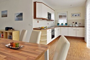 A modern kitchen with white cabinets, a microwave, and a sink. There is a dining table with chairs and a small bookshelf. - Vacation home with a fireplace, about 350 meters from the sandy beach, pets welcome (Glowe)