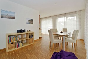 A dining area with a table and chairs, a bookshelf with books, and a window with curtains. - Vacation home with a fireplace, about 350 meters from the sandy beach, pets welcome (Glowe)