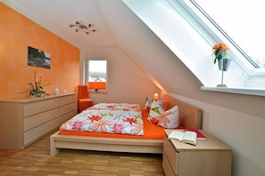 A bedroom with a skylight, a bed with floral bedding, a bedside table with a book, and a dresser. - Vacation home with a fireplace, about 350 meters from the sandy beach, pets welcome (Glowe)
