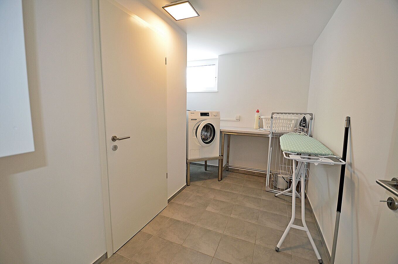 A laundry room with a washing machine, drying rack, and ironing station.